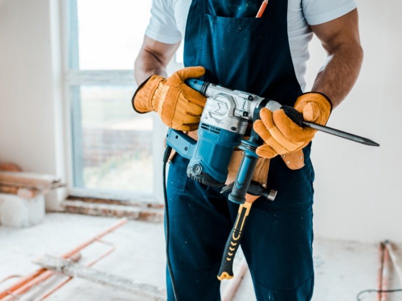 cropped view of workman in yellow gloves holding hammer drill