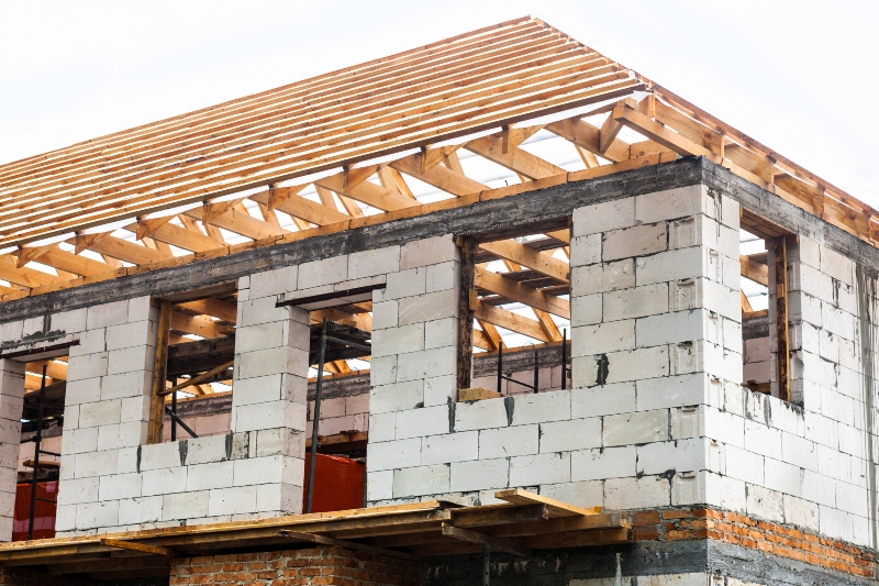 unfinished white brick house with timber roof truss.
